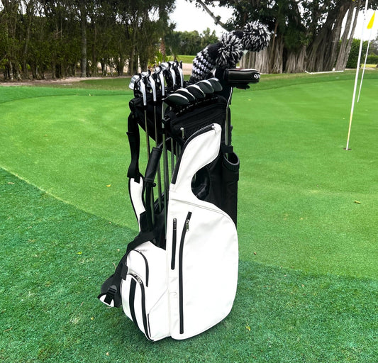 A lightweight white PU Leather NEVR LOOZ PRO CLIP CURV carry bag with clubs features iron and shaft clips for club organization, 2 putter tubes, 9 pockets, umbrella holder, towel holder, padded handle, rain hood, leg stand, and bottom cap on a golf course