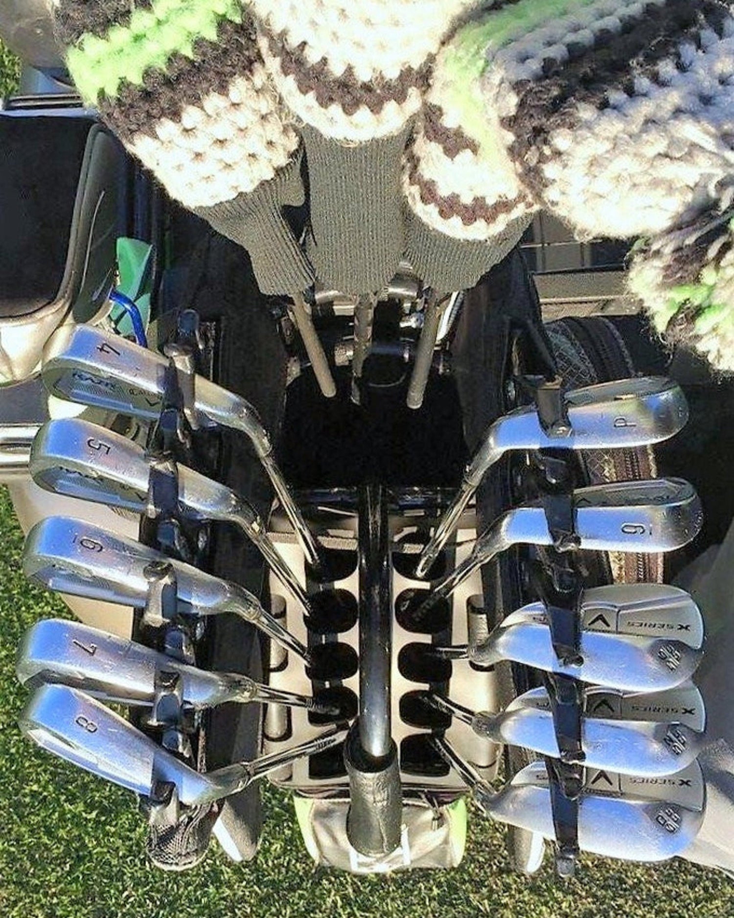 Set of golf clubs in a NEVR LOOZ golf bag with grass and car visible in the background.